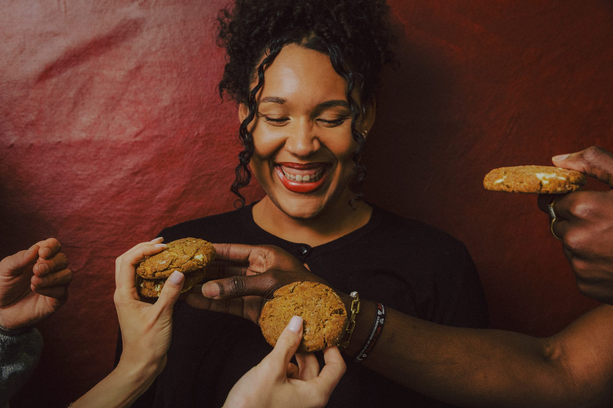 A woman laughing as friends offer her Ring & Robe cookies from every side